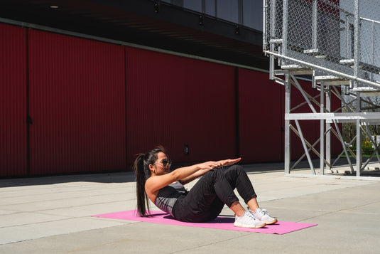 Woman on a pink yoga mat doing crunches by herself
